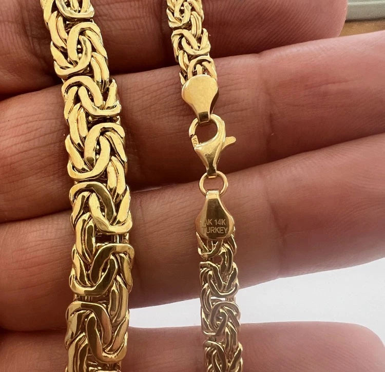 Gold chain necklace held by a hand with a clear background available on the TX.ORO website.