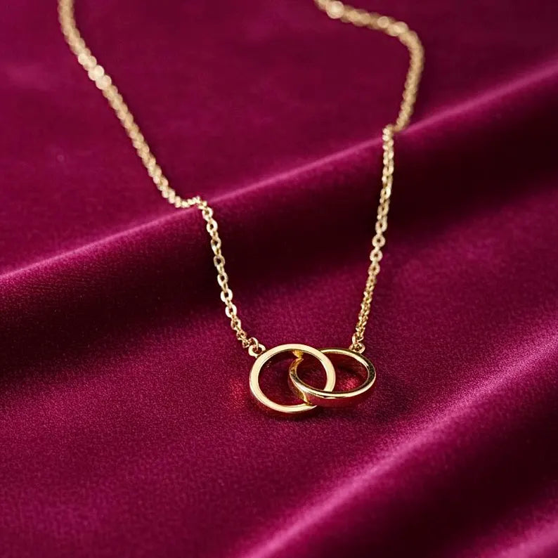 Gold necklace with interlocking rings on a purple fabric background available on the TX.ORO website.