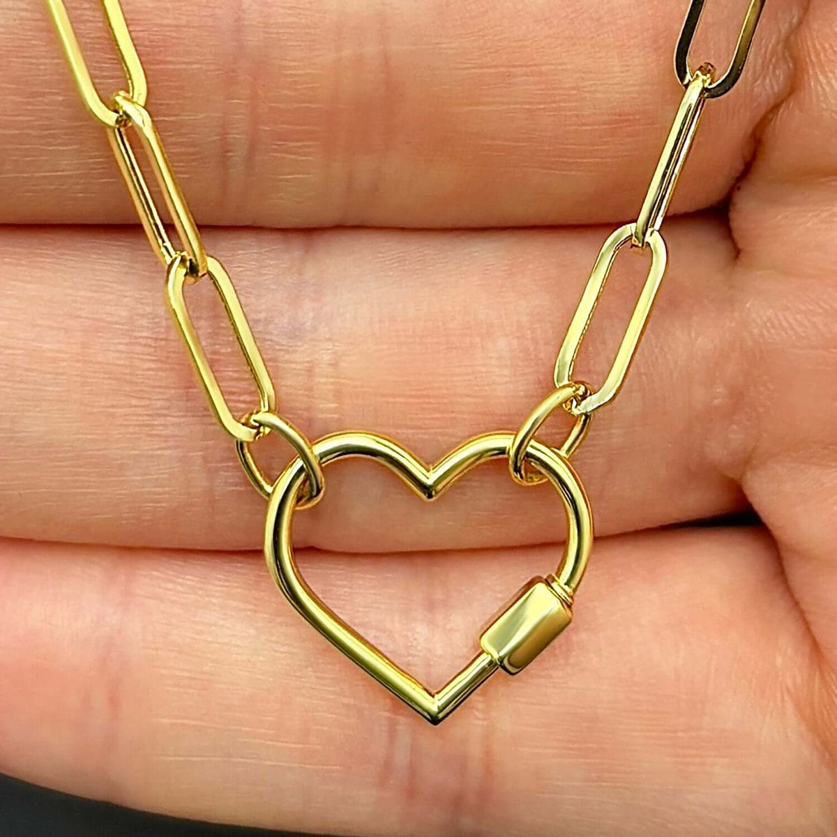 Gold heart-shaped necklace clasp on a hand available on the TX.ORO website.