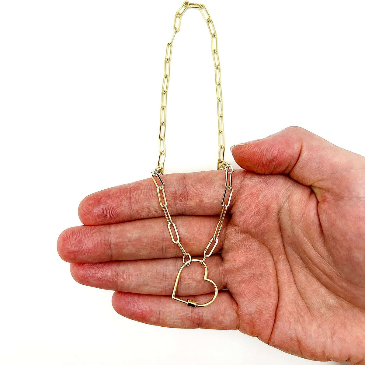 Gold chain necklace with a heart pendant held in a hand on a white background available on the TX.ORO website.