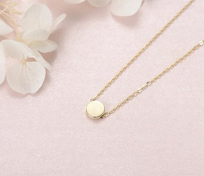 Gold necklace with a round pendant on a pink surface with white flowers available on the TX.ORO website.