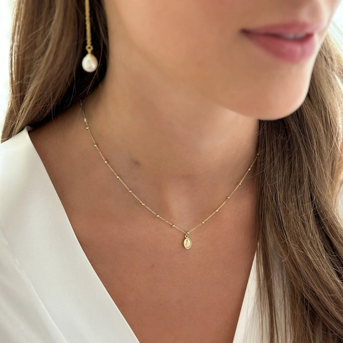Close-up of a woman wearing a gold necklace and pearl earring available on the TX.ORO website.
