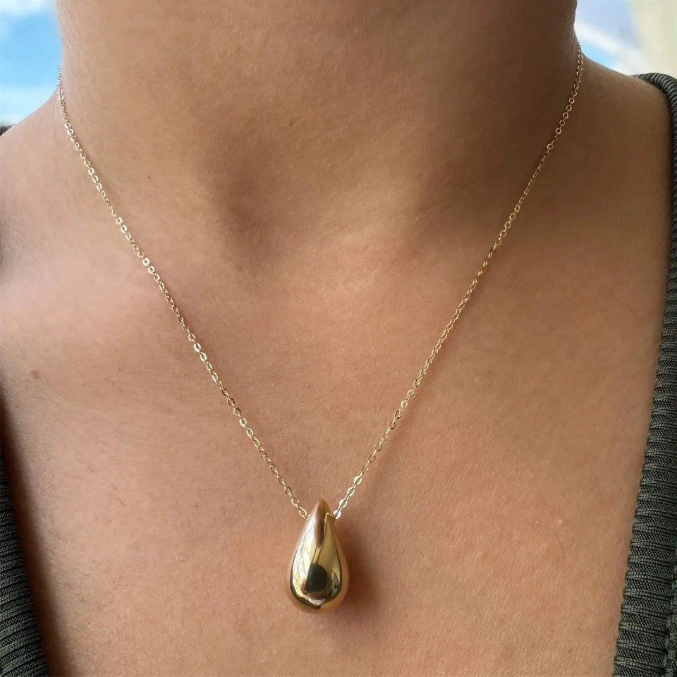 Gold necklace with a teardrop pendant on a person's neck against a blurred background available on the TX.ORO website.
