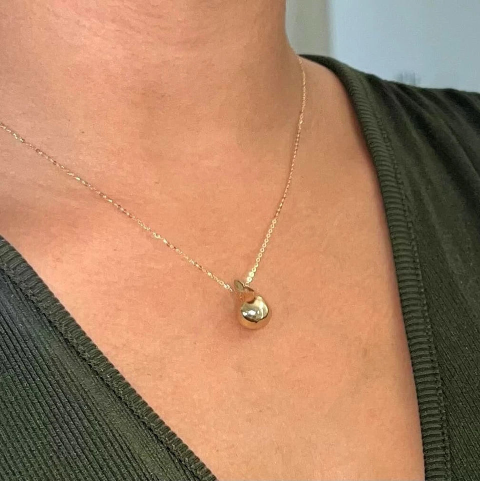 Gold necklace with a heart pendant worn by a person in an olive green top available on the TX.ORO website.