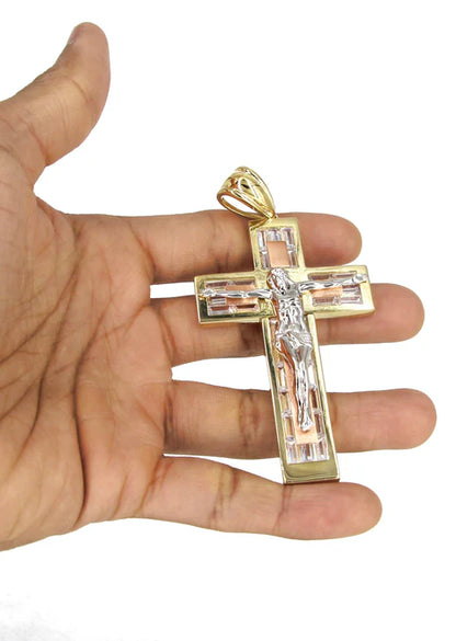 Gold cross pendant held in a hand against a white background available on the TX.ORO website.