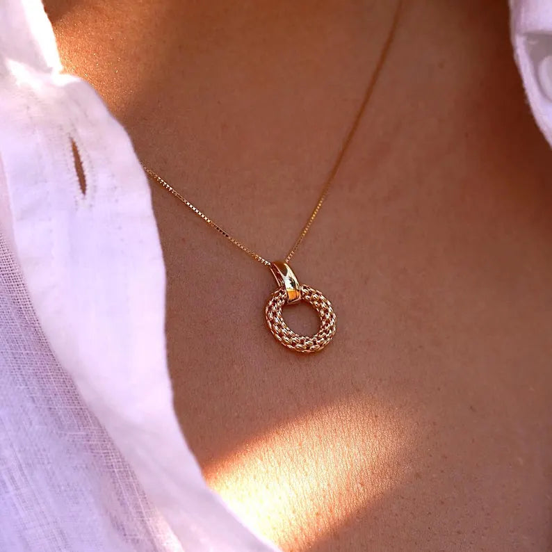 Gold necklace with a circular pendant on a person wearing a white shirt available on the TX.ORO website.