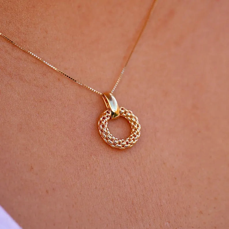 Gold necklace with a circular pendant on a person's neck against a neutral background available on the TX.ORO website.