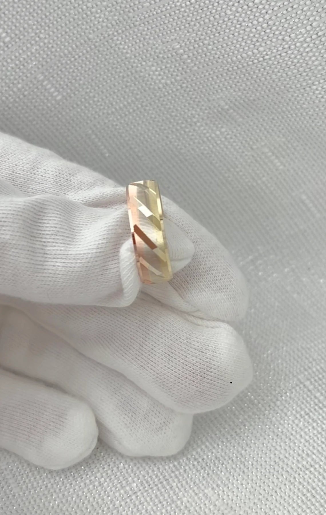 Gold ring on a white glove against a light gray background