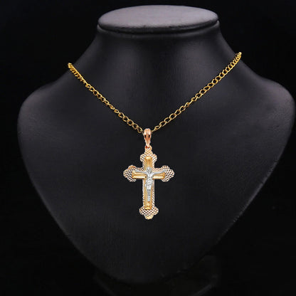 A gold cross pendant necklace with a textured beaded border and a central silver cross, displayed on a black jewelry bust against a black background.
