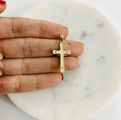 Gold cross pendant held between fingers on a marble surface