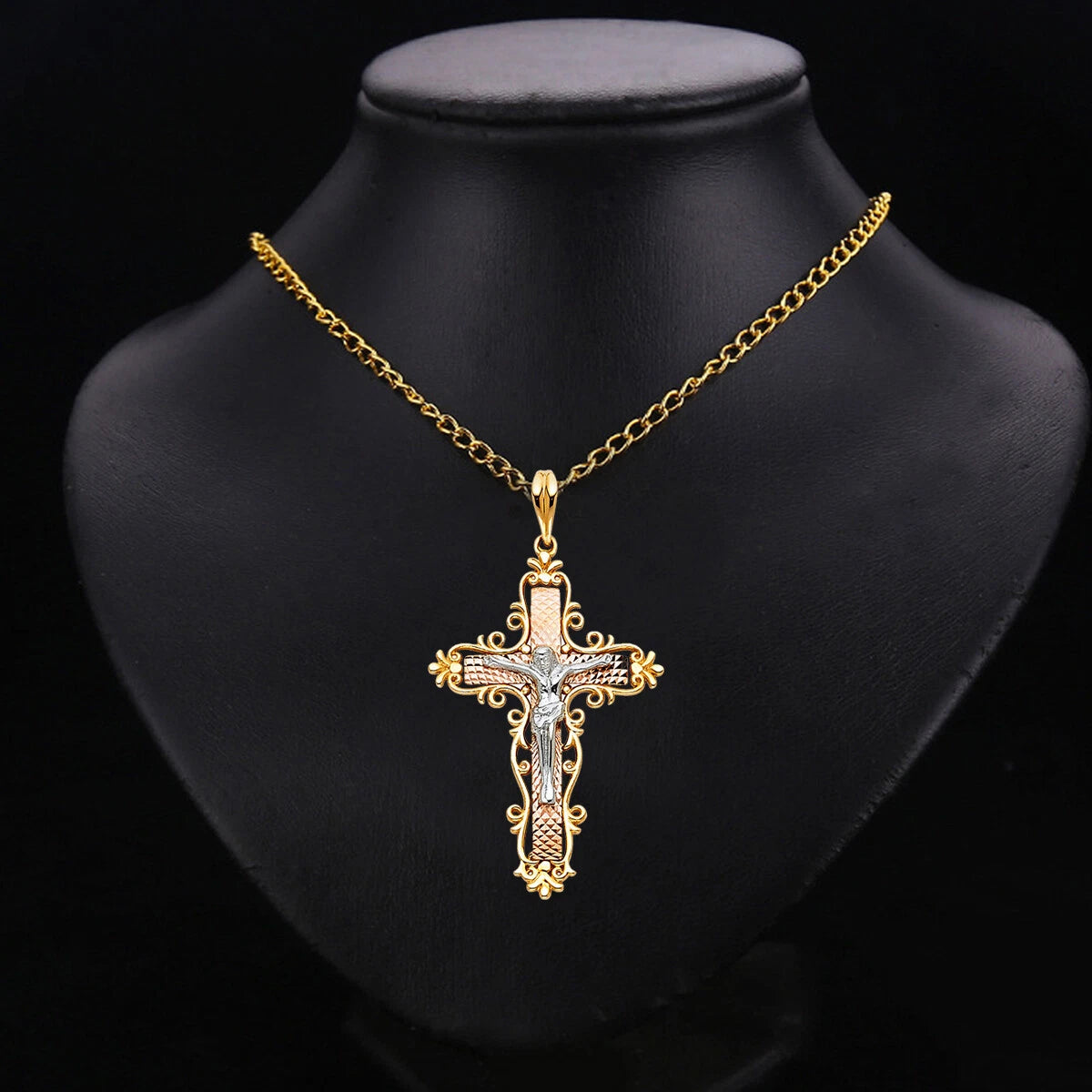 A gold cross pendant necklace with clear rhinestones, displayed on a black mannequin bust against a black background.