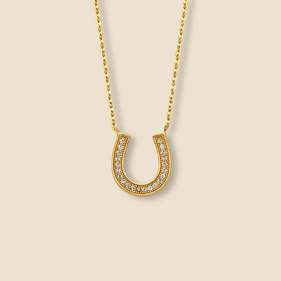 Gold horseshoe necklace with small diamonds on a beige background